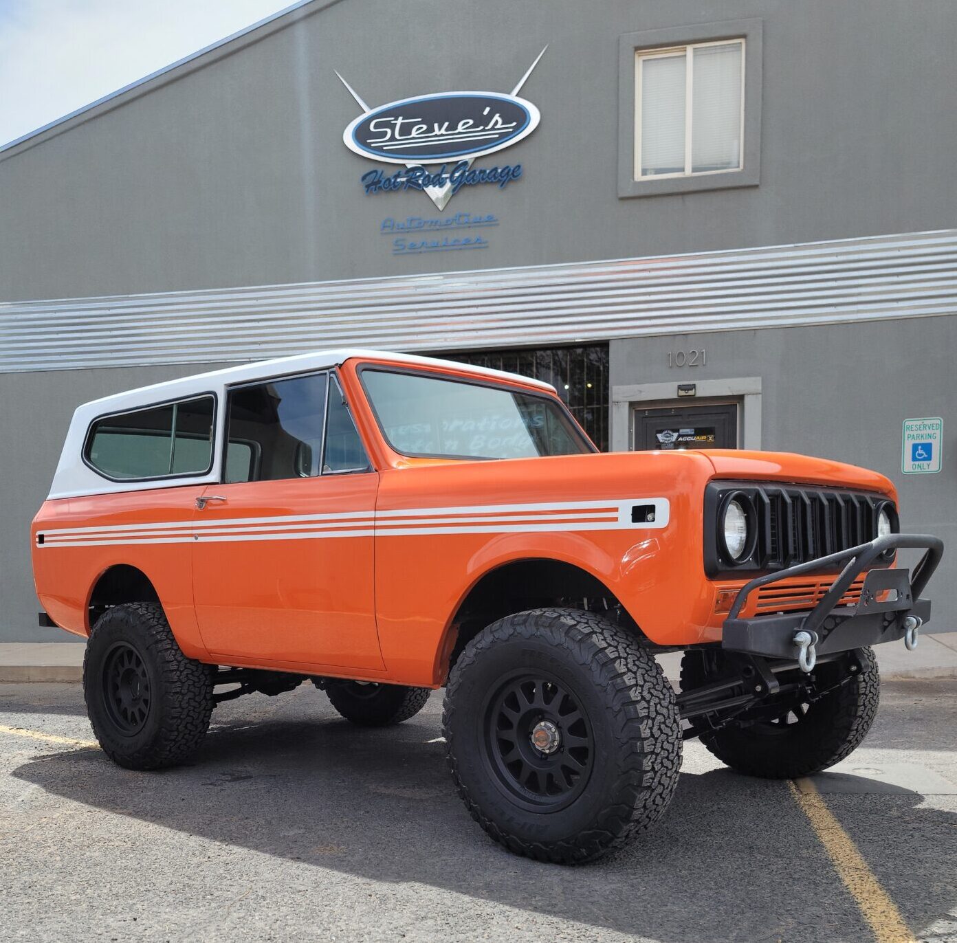 orange and white jeep parked in front of hot rod garage